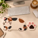 Hand tufted multicolor cat design keyboard wrist rest placed on a neat desk beside a matching paw shaped mouse pad, keyboard, coffee cup, notebook, and plant.